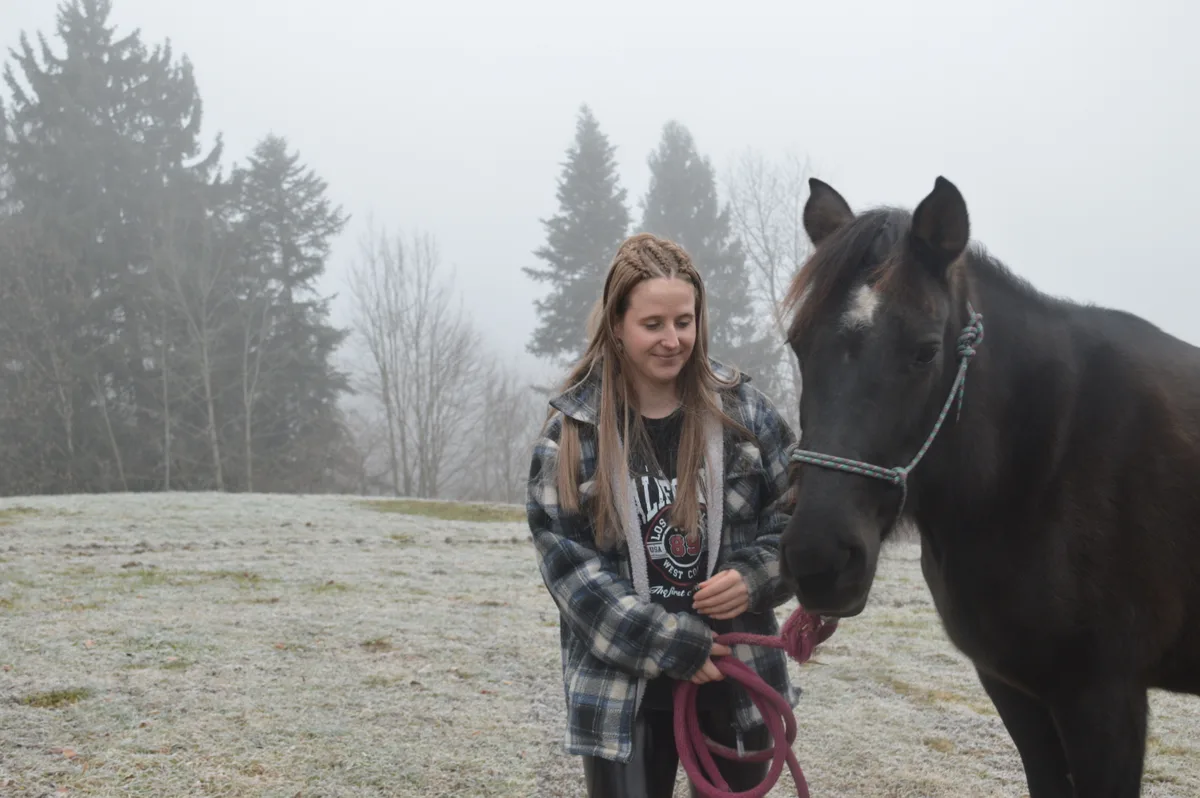 Eine Frau steht mit ihrem Pferd auf einer Wiese.